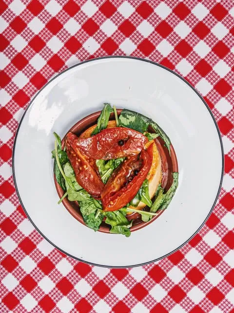 Plato con provoleta, tomates asados y hojas verdes sobre mantel a cuadros